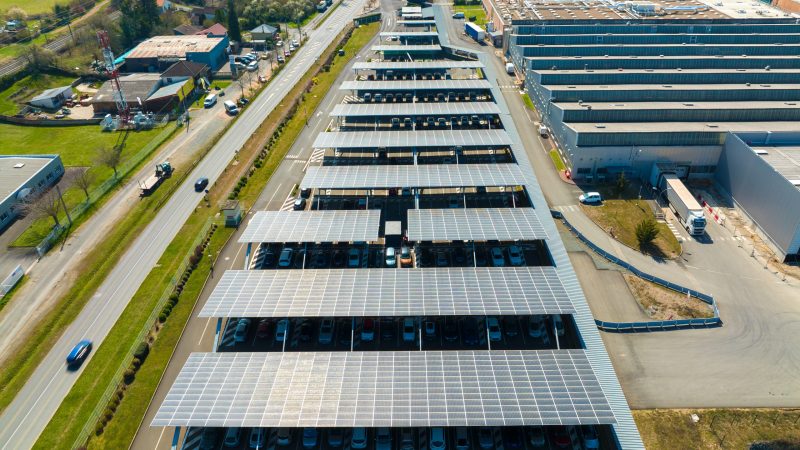 Aerial view of solar panels installed over parking lot with parked cars for effective generation of clean energy.
