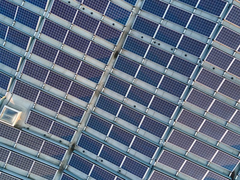 Aerial view of solar power plant with blue photovoltaic panels mounted on industrial building roof for producing green ecological electricity. Production of sustainable energy concept.