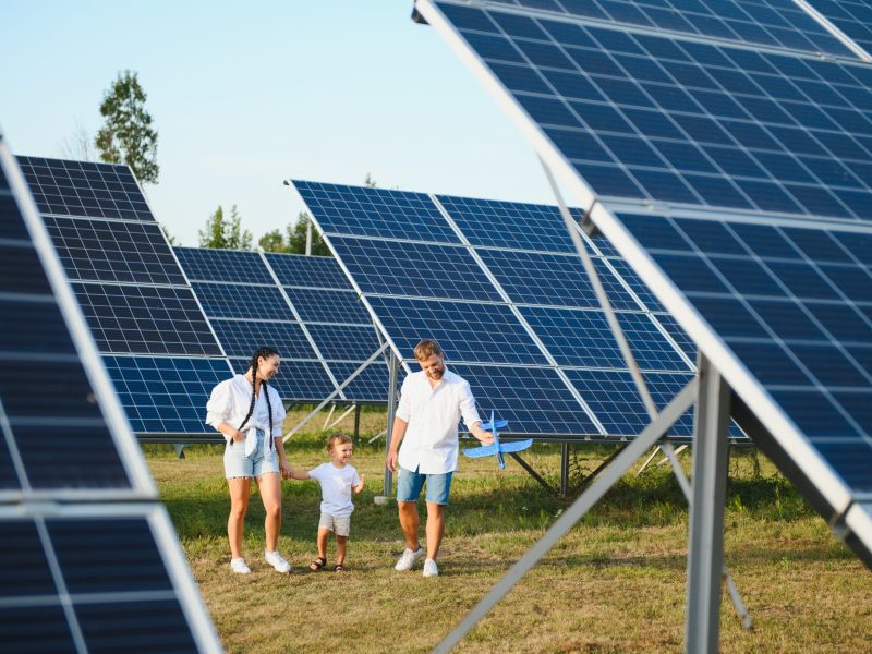 Enthusiastic father showing potential of alternative energy. Contemporary family looking at new solar station they bought. Side view of happy parents and interested child next to solar panels.